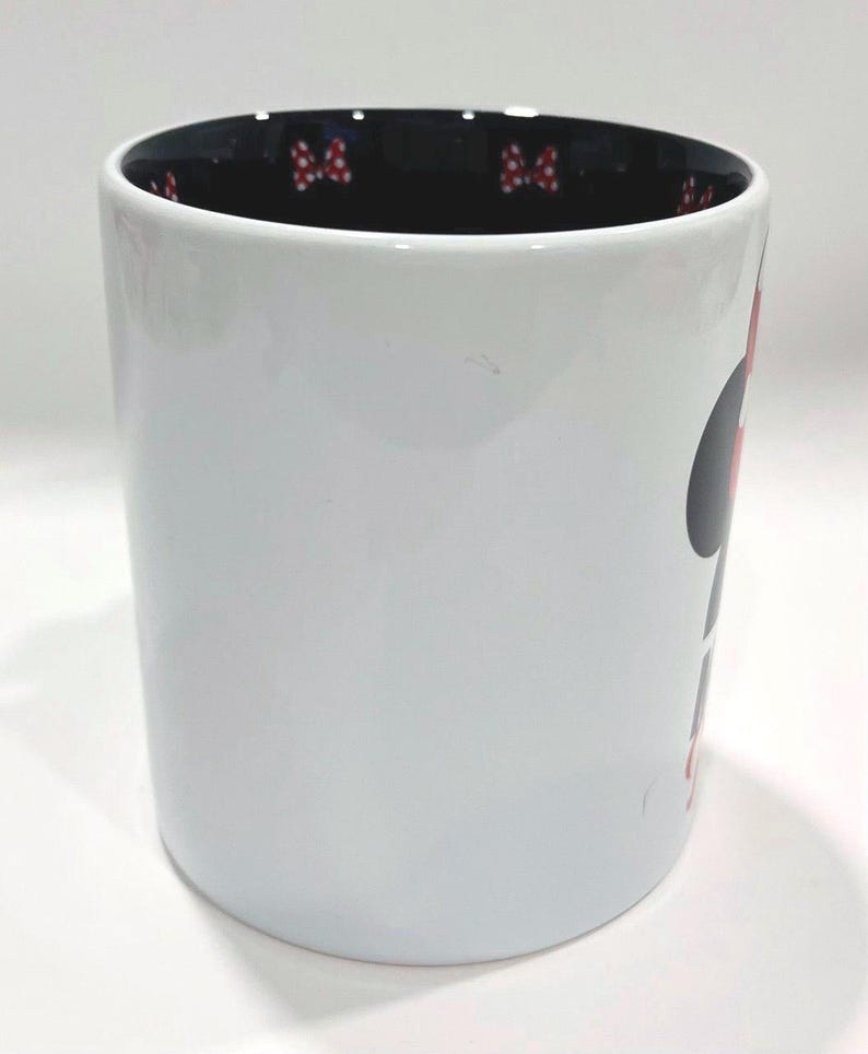 Puede incluir: Taza de cer&aacute;mica blanca con dise&ntilde;o de Minnie Mouse. La taza tiene un interior negro con detalles de lazo rojo. Una gran silueta de Minnie Mouse est&aacute; en el lateral.
