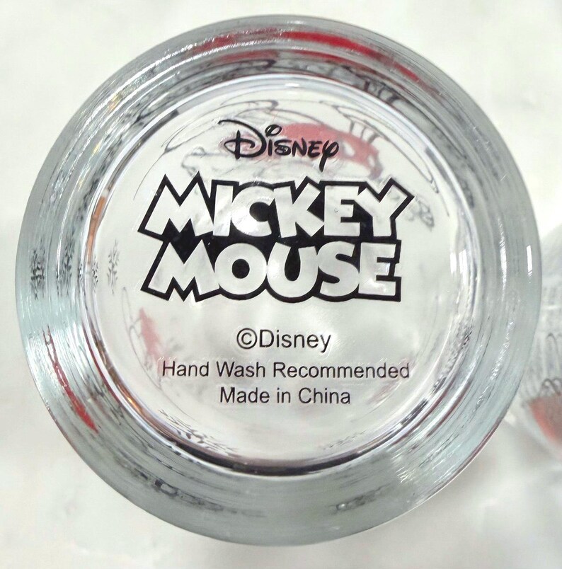 Pu&ograve; includere: Bicchiere trasparente con le parole "Disney MICKEY MOUSE" in bianco e nero. Il fondo del bicchiere include anche il logo Disney e il testo "Hand Wash Recommended Made in China."