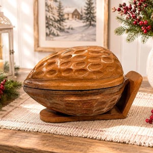 Könnte beinhalten: Eine braune Holzschale in Form einer großen Walnussschale mit einer texturierten, genoppten Oberfläche. Die Schale ruht auf einem passenden Holzsockel, der die geschwungene Form stützt und eine glatte Oberfläche sowie eine natürliche Holzmaserung aufweist.