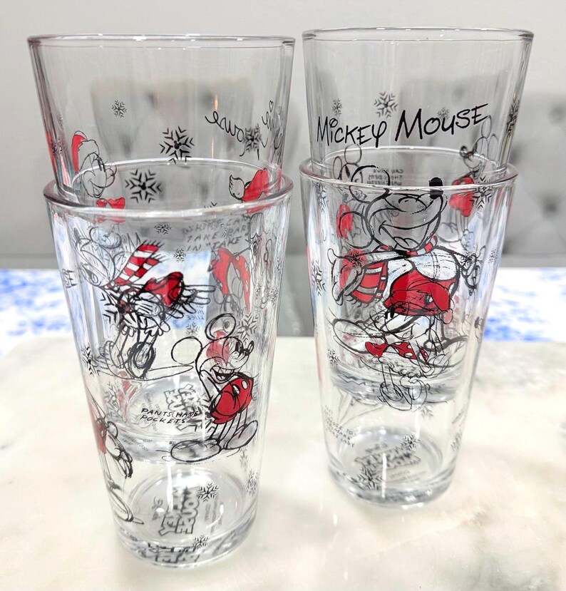 Pu&ograve; includere: Set di quattro bicchieri trasparenti con disegni invernali di Topolino. Ogni bicchiere presenta una diversa illustrazione di Topolino in rosso, nero e bianco, con fiocchi di neve e la scritta "Mickey Mouse" su alcuni.