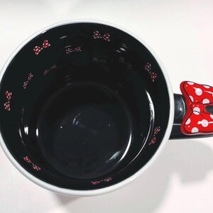 Puede incluir: Taza de cer&aacute;mica negra con borde blanco y asa en forma de lazo rojo. El interior es negro con peque&ntilde;os lazos rojos. El asa es un lazo rojo con lunares blancos. Un dise&ntilde;o divertido y caprichoso.