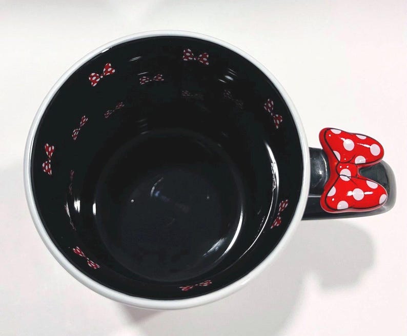 Puede incluir: Taza de cer&aacute;mica negra con borde blanco y asa en forma de lazo rojo. El interior es negro con peque&ntilde;os lazos rojos. El asa es un lazo rojo con lunares blancos. Un dise&ntilde;o divertido y caprichoso.