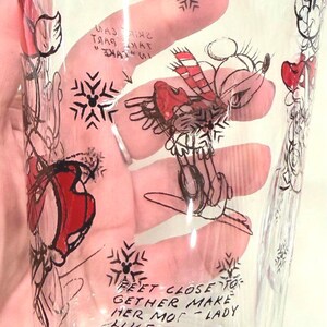 Pu&ograve; includere: Bicchiere trasparente con un disegno a mano di un personaggio di topo con cappello e sciarpa rossi, e fiocchi di neve. Il bicchiere ha la parola "Mouse" e il testo "Feet close to gether make her mot-lady like".