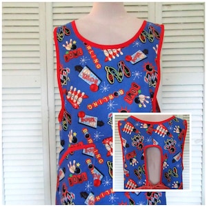 May include: A blue bowling-themed apron with red trim and pockets. The apron features a repeating pattern of bowling pins, balls, and the word "BOWLING". The apron has a scoop neck and a keyhole back.