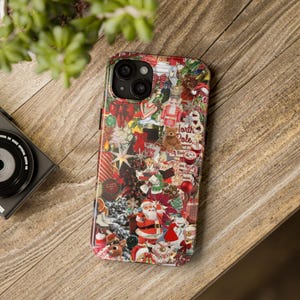 May include: A colorful phone case with a collage of Christmas-themed images, including Santa Claus, reindeer, and candy canes. The case is on a wooden surface, with a camera and greenery in the background.