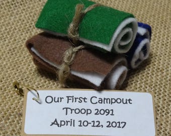 May include: A felt craft of three rolled-up sleeping bags tied together with twine. The label reads "Our First Campout Troop 2091 April 10-12, 2017".