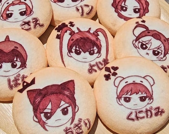 Puede incluir: Una colección de galletas redondas y claras dispuestas en un plato de madera. Cada galleta presenta una ilustración de personaje de estilo anime diferente en tonos rojos y negros, con texto japonés. Las galletas tienen una superficie ligeramente texturizada.