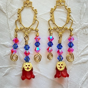 May include: Gold filigree earrings with dangling red, pink, and blue crystal beads. The earrings have a bell-shaped charm at the bottom.
