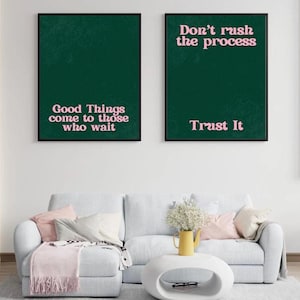 May include: Two framed art prints with dark green backgrounds and pink text. One reads "Good Things come to those who wait," and the other says "Don't rush the process, Trust It." The prints hang above a white sofa with pink pillows.
