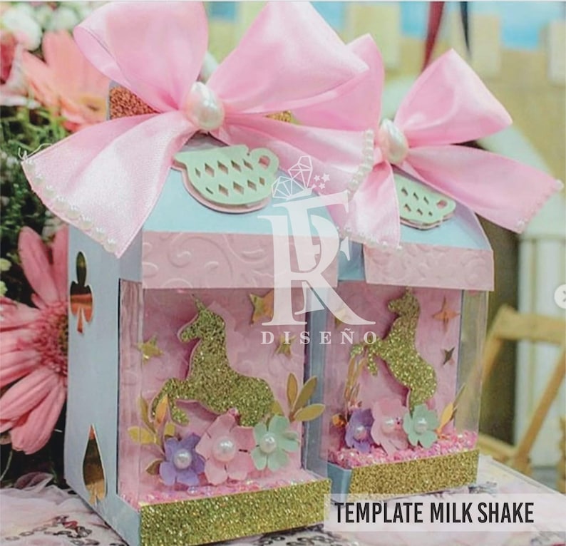 Pode incluir: Duas caixas decorativas em azul claro e rosa, com um design de unic&oacute;rnio. Cada caixa tem um grande la&ccedil;o rosa e uma p&eacute;rola. As caixas t&ecirc;m uma base dourada brilhante e o texto "TEMPLATE MILK SHAKE".