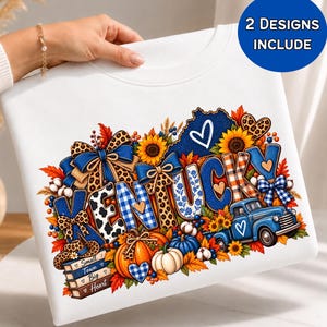 May include: A white sweatshirt featuring a colourful graphic with the word KENTUCKY in blue and patterned letters. The design includes sunflowers, pumpkins, a blue truck, bows, and a stack of books labelled Small Town Big Heart, all accented with hearts.