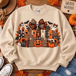 Puede incluir: Una sudadera beige de cuello redondo con un estampado gráfico que incluye el texto HALLOWEEN MOM. El diseño presenta calabazas, girasoles, fantasmas, murciélagos, telarañas y lazos con patrones en naranja, negro y estampado de leopardo.