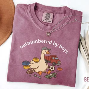 Berry Comfort Colors shirt with “outnumbered by boys” text and cute goose with toys illustration