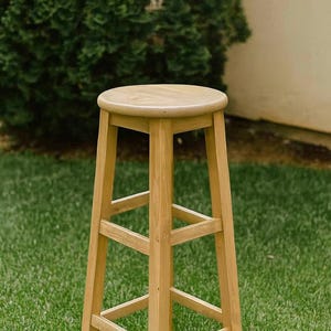 May include: A tall, wooden bar stool with a round seat and four sturdy legs. The stool is made of light-colored wood and features a simple, classic design. The stool is approximately 30 inches tall.