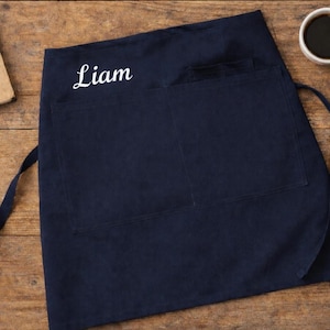 Op de afbeelding: Een set van drie keramische mokken met een gespikkelde, cr&egrave;mekleurige glazuur. Elke mok heeft een ander handgeschilderd ontwerp: een blauw en groen blad, een gele bloem en een rode bes. De mokken hebben een eenvoudige, afgeronde vorm.