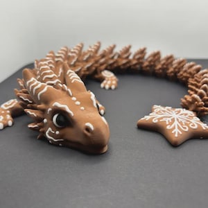 May include: A brown dragon figurine with white accents and a star-shaped piece. The dragon has a detailed design with a long, curved tail. The star has a white snowflake design. The figurine is on a dark surface.