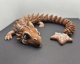 May include: A brown dragon figurine with white accents and a star-shaped piece. The dragon has a detailed design with a long, curved tail. The star has a white snowflake design. The figurine is on a dark surface.