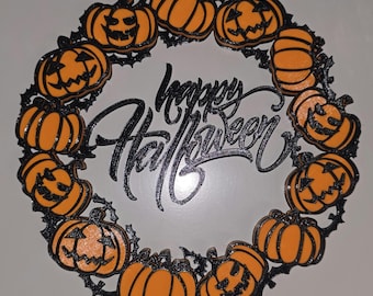 May include: A circular wall decoration featuring a ring of orange jack-o'-lanterns and plain pumpkins connected by black vine-like structures. In the center, the text "happy Halloween" is written in a black, cursive, stylized script font.