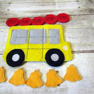 May include: A yellow felt toy school bus with black wheels and windows. The bus has five red felt "STOP" signs on top and six orange felt bells below.