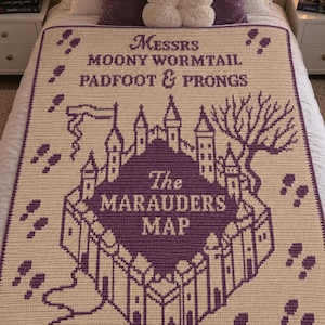Könnte beinhalten: Eine cremefarbene Häkeldecke mit violettem Text und einer Schlossgrafik. Der Text lautet: MESSRS MOONY WORMTAIL PADFOOT & PRONGS und The MARAUDERS MAP. Das Design enthält violette Fußabdrücke, die über die Oberfläche der Decke verteilt sind.