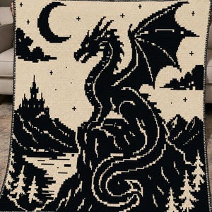 May include: A rectangular crochet blanket featuring a high-contrast black and cream pixelated design. The scene depicts a large dragon perched on a rocky cliff overlooking a lake, with a castle, pine trees, a crescent moon, and stars in the sky.