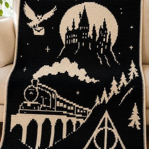 Può includere: Una coperta all'uncinetto nera e crema che raffigura la sagoma di un grande castello davanti a una luna piena, un treno a vapore su un ponte, un gufo in volo con una lettera, una foresta di pini e un simbolo triangolare con cerchio e linea.
