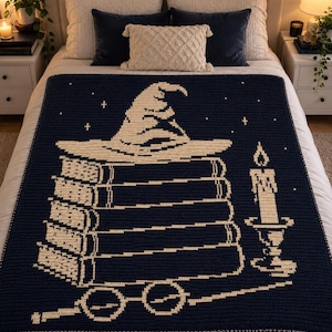 May include: A dark navy blue crochet blanket featuring a cream-colored graphic design. The pattern depicts a pointed hat resting on a stack of four books, accompanied by a lit candle in a holder and a pair of round glasses positioned at the bottom.