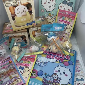May include: A collection of Chikawa character merchandise including several boxed figures, small plastic-wrapped interior mascot figurines, colorful acrylic keychains, and a blue plastic folder featuring a cartoon character with a shopping cart.