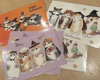 Puede incluir: Una colección de tarjetas de felicitación rectangulares con ilustraciones de gatos mofusand con temas de Halloween. Las tarjetas muestran gatos disfrazados, con sombreros de bruja y calabazas, con el texto Happy Halloween y Boo! en varios colores.