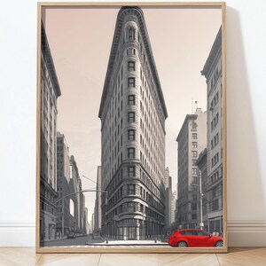 May include: A framed print of the Flatiron Building in New York City. The artwork is in black and white, with a red car parked on the street. The print is in a light wood frame.