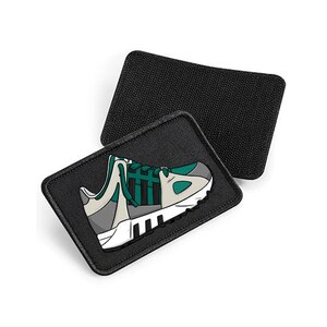 May include: Two rectangular black patches with hook-and-loop backing. The top patch is plain black, while the bottom patch features a graphic illustration of a sneaker in shades of teal, grey, white, and black with three prominent black stripes.