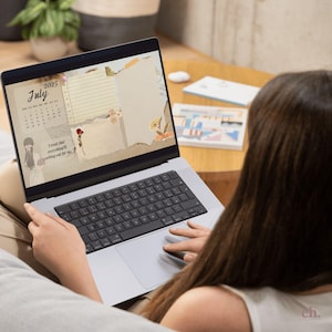 May include: A laptop displaying a digital planner for July 2025. The planner features a calendar, floral accents, and the quote "I trust that everything's working out for me." The laptop is open on a person's lap.