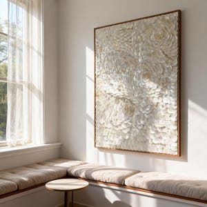 May include: A large, rectangular wall art piece with a wooden frame. The artwork features a textured, three-dimensional design of white, petal-like elements arranged in a floral pattern. The piece is mounted on a white wall, near a window.