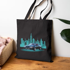 Könnte beinhalten: Schwarze Tragetasche mit einer türkisfarbenen Skyline-Grafik und einem dunkelblauen Sportwagen. Das Auto ist auf einem türkisfarbenen Scheinwerfer zentriert, mit der Stadtsilhouette im Hintergrund. Die Tasche hat schwarze Griffe.
