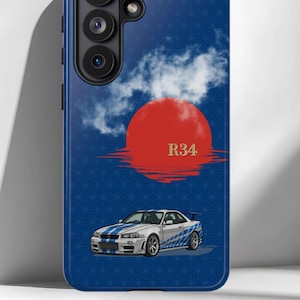 以下が含まれることがあります： 青いスマートフォンケース。青いレーシングストライプが入った白いR34スポーツカーが描かれています。デザインには、大きな赤い太陽、白い雲、金色のR34の文字が含まれており、幾何学模様のダークブルーの背景に配置されています。