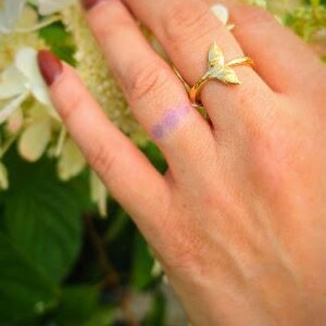 May include: A gold-toned ring featuring a stylized whale tail or mermaid fin design. The band is thin and polished, with the fin motif extending upward from the center. The ring is worn on a finger, showcasing the metallic finish and shape.