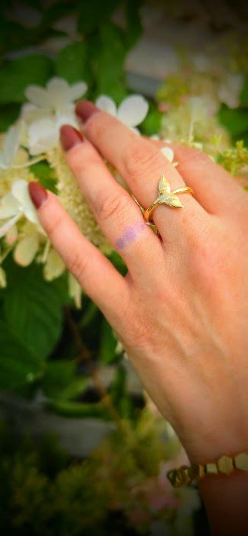 May include: A gold-toned ring featuring a stylized whale tail or mermaid fin design. The band is thin and polished, with the fin motif extending upward from the center. The ring is worn on a finger, showcasing the metallic finish and shape.