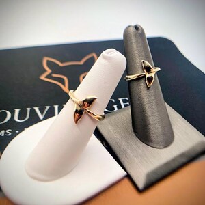 May include: Two gold rings, each featuring a delicate whale tail design. The rings are displayed on individual finger-shaped stands, one white and one dark gray, showcasing the polished metallic finish and the curved shape of the whale tail motif.