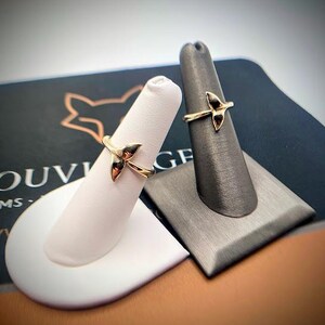 May include: Two gold rings, each featuring a whale tail design. The rings are displayed on individual finger-shaped stands, one white and one dark gray, positioned against a dark background with partial text visible.