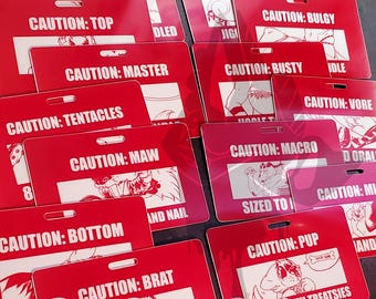 Könnte beinhalten: Eine Sammlung roter PVC-Kunststoffausweise mit verschiedenen "CAUTION"-Warnungen und Cartoon-Illustrationen. Die Ausweise zeigen Texte wie "SWITCH", "BOOTY", "MASTER" und "PUP". Der Text "PVC Plastic Badges" ist ebenfalls sichtbar.