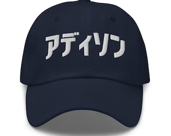 Könnte beinhalten: Eine marineblaue Baseballkappe mit weißem, gesticktem japanischem Katakana-Text, der auf der Vorderseite アディソン lautet. Die Kappe verfügt über eine strukturierte Krone, einen gebogenen Schirm und einen Knopf in der Mitte der Oberseite.