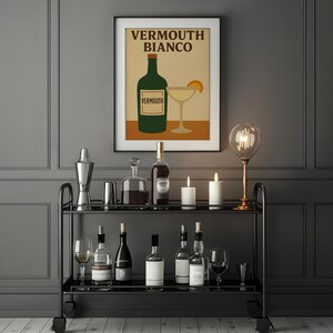 Può includere: Un carrello bar nero con varie bottiglie di liquore, bicchieri, uno shaker e candele. Un poster incorniciato con le parole "Vermouth Bianco" e un'illustrazione di bottiglia verde è appeso al muro.