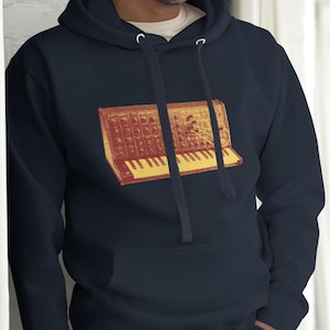 May include: Navy blue hoodie featuring a retro synthesizer graphic in shades of red and yellow. The hoodie has a drawstring hood and a front pocket. The graphic is centered on the chest.
