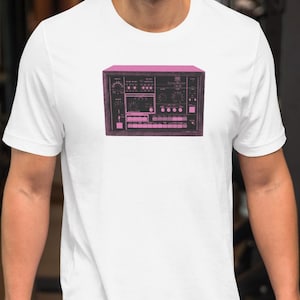 May include: White t-shirt featuring a pink graphic of a vintage stereo receiver. The design includes knobs, buttons, and a display, giving it a retro aesthetic. The shirt is made of a soft material and is suitable for casual wear.