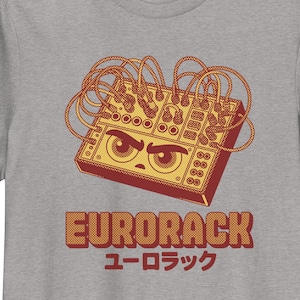 Puede incluir: Camiseta gris con una ilustración de dibujos animados de un módulo de sintetizador Eurorack con una cara enfadada. El diseño incluye la palabra "EURORACK" en una fuente retro, con texto japonés debajo.