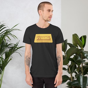 May include: Black t-shirt featuring a yellow graphic of a TR-808 drum machine. The design includes the text "TR-808" at the top. The shirt is a short-sleeved crew neck style.