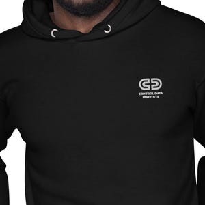 Op de afbeelding: Zwarte hoodie met een wit logo op de borst. Het logo toont de letters "CD" boven elkaar, met daaronder de woorden "CONTROL DATA INSTITUTE". De sweatshirt heeft een capuchon met trekkoord en een voorzak.