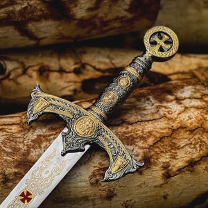 May include: An ornate sword with a silver blade and gold accents. The hilt features intricate designs and a cross-shaped emblem. The sword rests on a wooden surface, showcasing its detailed craftsmanship and historical aesthetic.