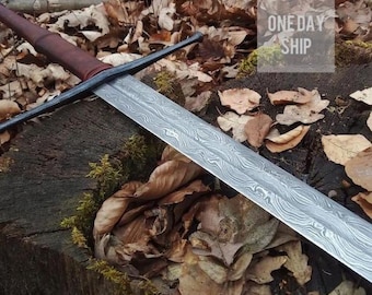 May include: A long sword with a double-edged blade featuring a distinct wavy, layered metal pattern. The sword has a dark, straight crossguard and a brown leather-wrapped handle. The text "ONE DAY SHIP" is visible in the upper right corner.