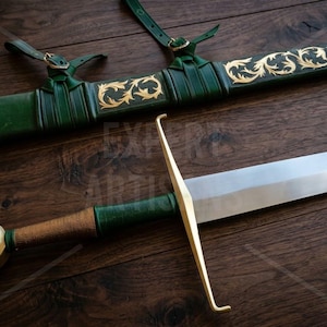 May include: A sword with a silver blade, a gold crossguard, and a green leather-wrapped handle with a gold pommel. Beside it lies a matching green leather scabbard featuring gold filigree scrollwork and two leather attachment straps.
